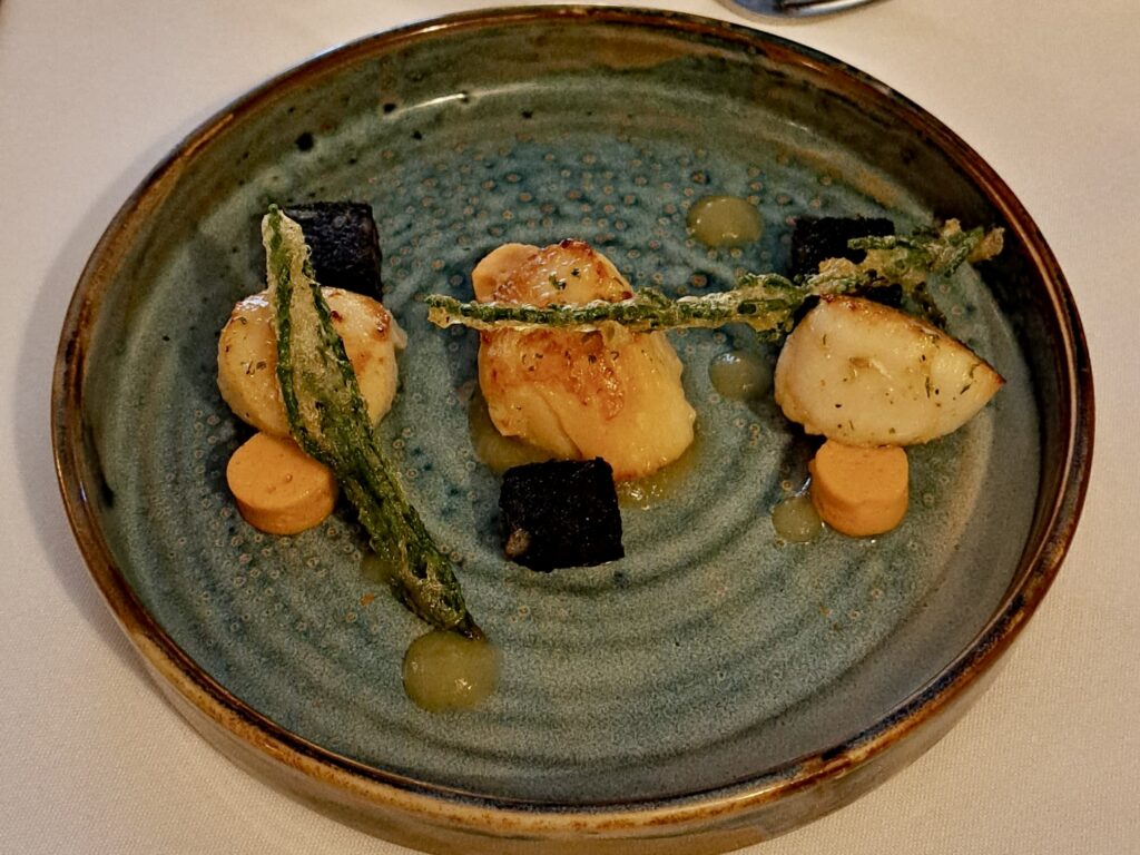 Scallops sat on a blue plate with decorative food accents